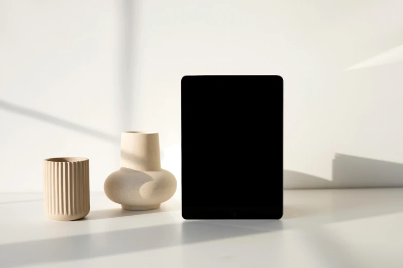 a cell phone sitting on top of a table next to a vase, a computer rendering, all black matte product, ignant, ipad pro, product introduction photo