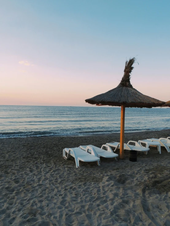 a group of lounge chairs sitting on top of a sandy beach, marbella, profile image, sunset view, parasol