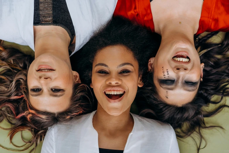 a couple of women laying on top of a bed, trending on pexels, three heads, symmetrical face happy, upside-down, crooked teeth