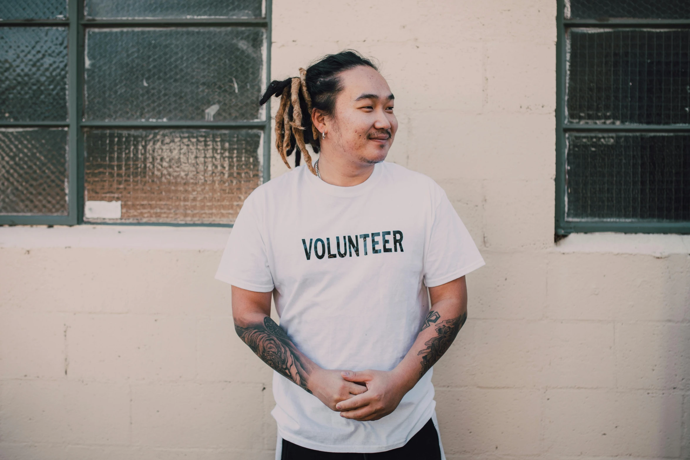 a man with dreadlocks standing in front of a building, inspired by Juan Villafuerte, pexels contest winner, printed on a cream linen t-shirt, andy milonakis, nanae kawahara, bringing people together