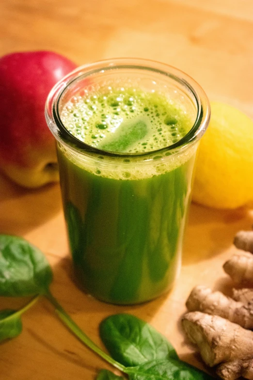 a glass of green juice sitting on top of a wooden table, ginger, “organic, vibrant colour, green robe