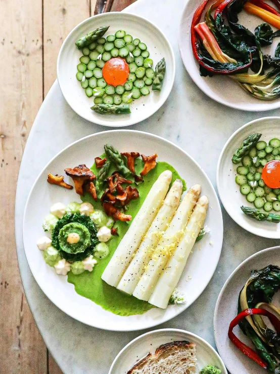 a table topped with plates of food on top of a wooden table, inspired by Géza Dósa, asparagus, instagram photo, zinc white, vibrant green