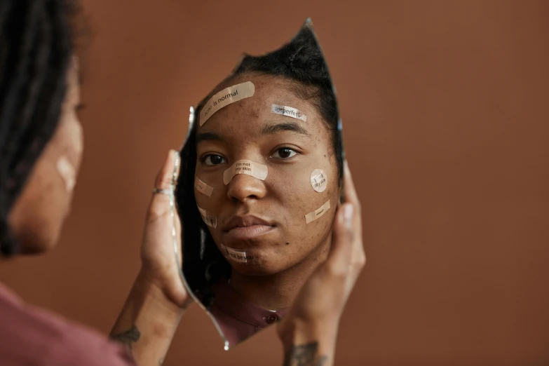 a woman with tape on her face looking in a mirror, trending on pexels, hyperrealism, brown skin like soil, thumbnail, studio photo, markings on her face