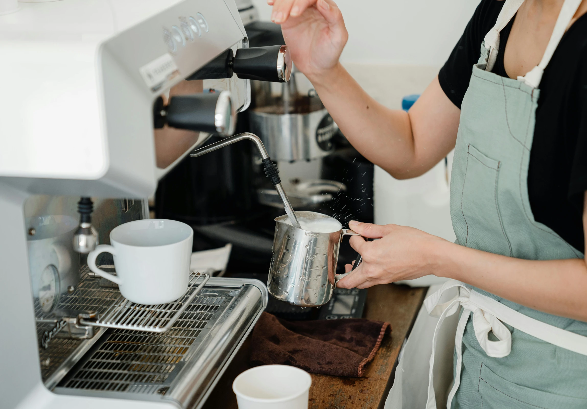 a woman preparing a cup of coffee in a kitchen, by Nick Fudge, pexels contest winner, aussie baristas, white apron, espresso machine, where a large