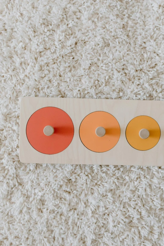 a wooden toy sitting on top of a white carpet, inspired by Frederick Hammersley, unsplash, color field, the three suns, birch, grey orange, circular