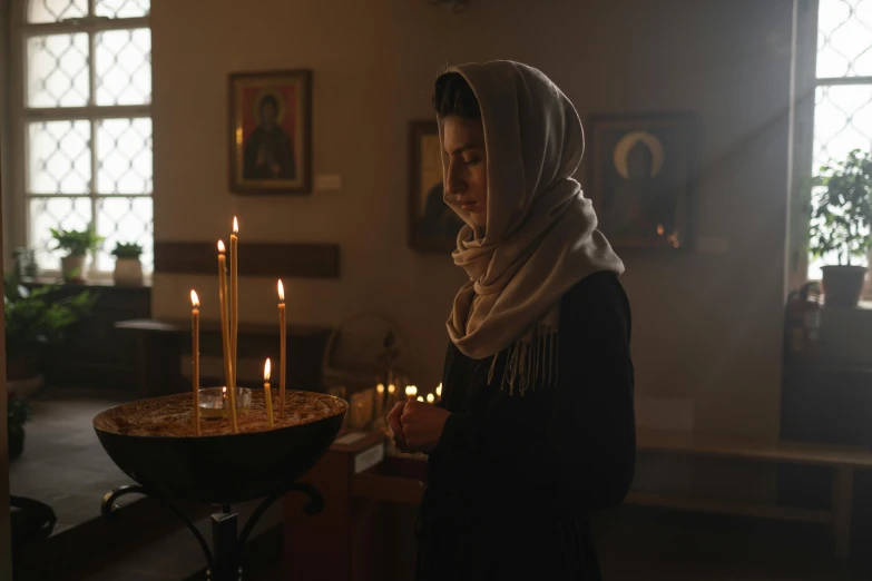a woman is lighting candles in a church, a portrait, pexels, hurufiyya, nun outfit, moviestill, profile image, modest