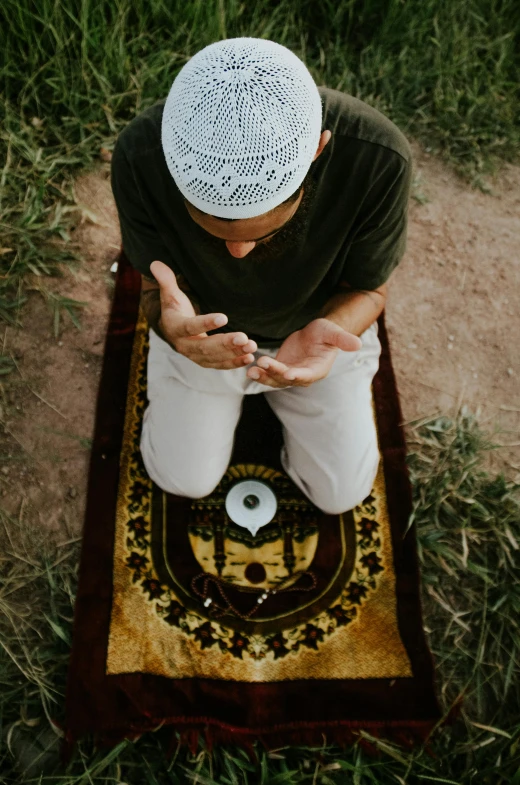 a man sitting on top of a rug in the grass, doing a prayer, spell casting, instagram post, mosque