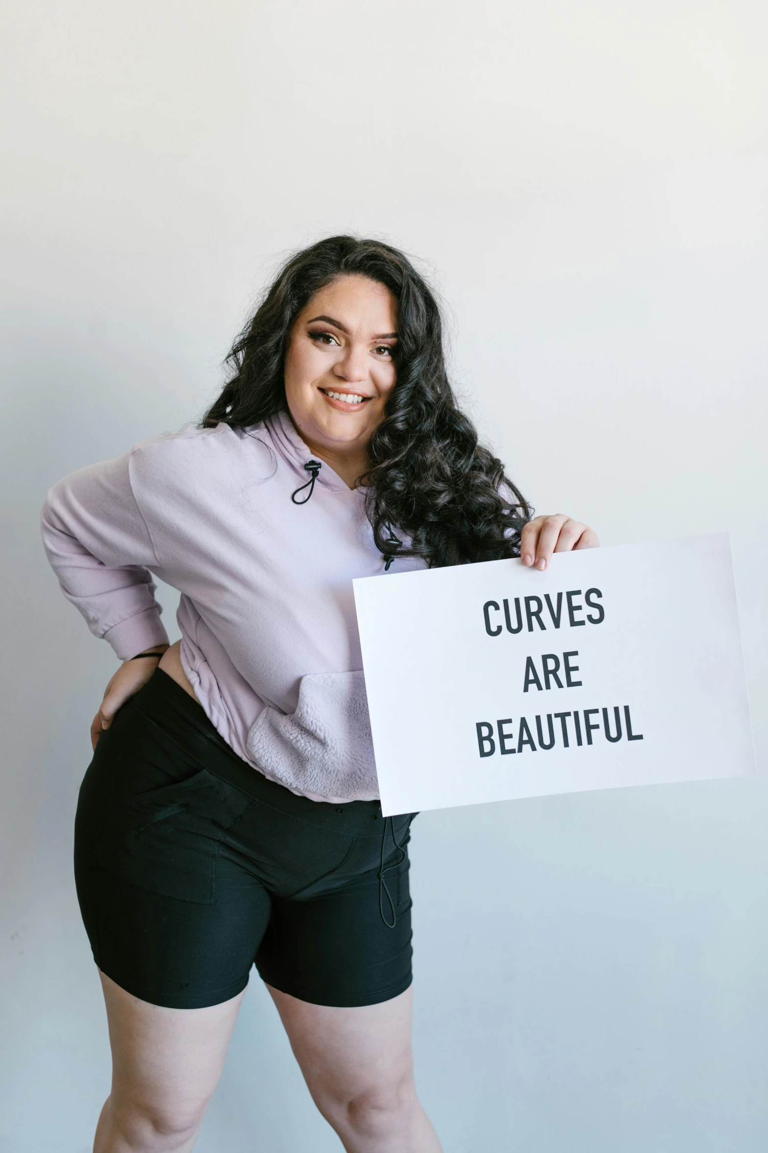 a woman holding a sign that says curves are beautiful, pexels contest winner, alanis guillen, looking to the side, curvy build, on a canva