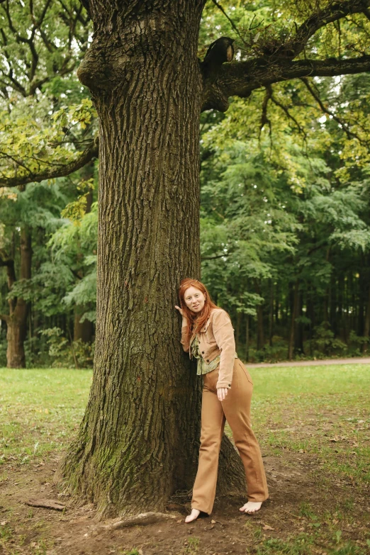 a woman leaning against a tree in a park, inspired by Elsa Bleda, trending on pexels, renaissance, brown pants, ( redhead, taken with kodak portra, portrait of tall