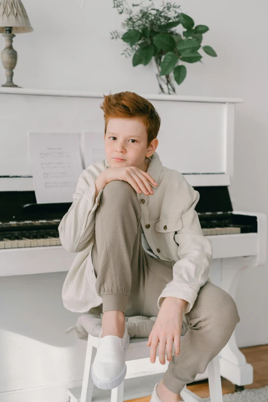 a man sitting on a stool in front of a piano, inspired by Aleksander Gine, trending on pexels, red haired teen boy, wearing white pajamas, muted colors. ue 5, portrait androgynous girl