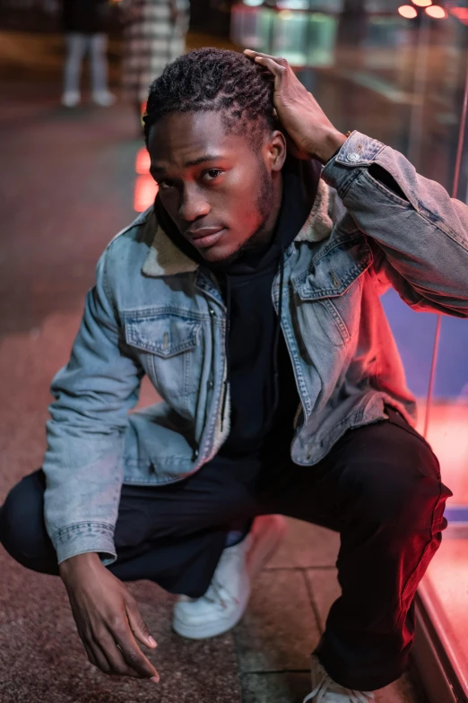 a man leaning against a wall with his hand on his head, an album cover, by Cosmo Alexander, trending on pexels, wearing a jeans jackets, hero pose colorful city lighting, ( ( dark skin ) ), androgynous person