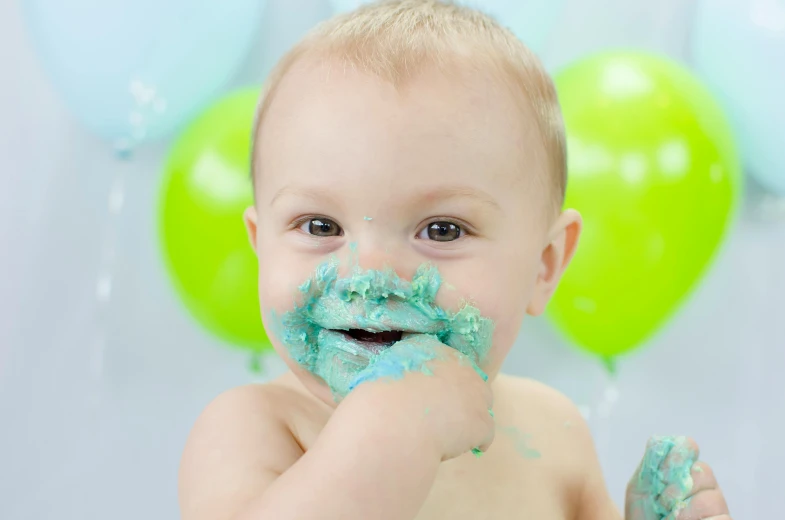 a baby sitting in front of a cake covered in blue icing, pexels, skin painted with green, spitting cushions from his mouth, on grey background, green sparkles