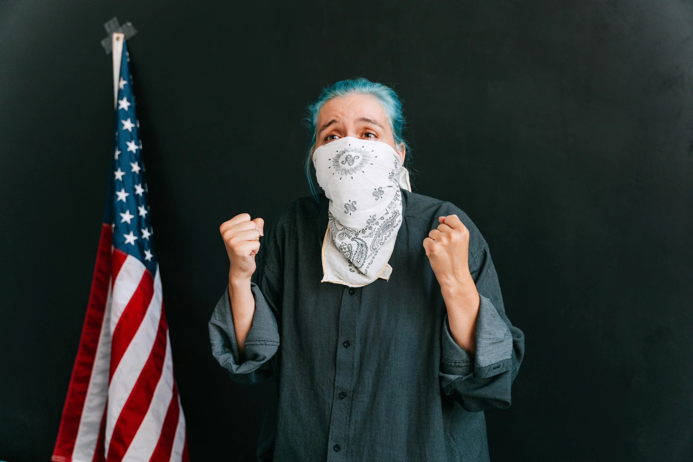 a man wearing a face mask in front of an american flag, a colorized photo, pexels contest winner, portraits of a woman enraged, bandana, standing with a black background, girl with blue hair