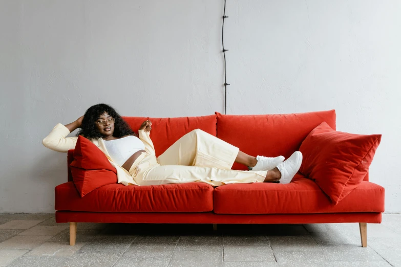 a woman sitting on top of a red couch, trending on pexels, lined in cotton, lounge furniture, maria borges, fullbody view