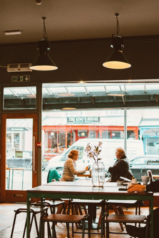 a group of people sitting at a table in a restaurant, by Anna Findlay, unsplash, award winning shopfront design, facing each other, holywood scene, city morning