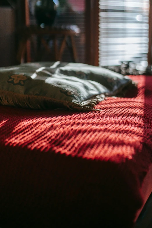 a red bed sitting in a bedroom next to a window, unsplash contest winner, dappled afternoon sunlight, carpeted floor, evening sun, low-angle