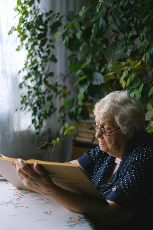 a woman sitting at a table reading a book, a portrait, pexels contest winner, nursing home, gardening, gif, backlighted