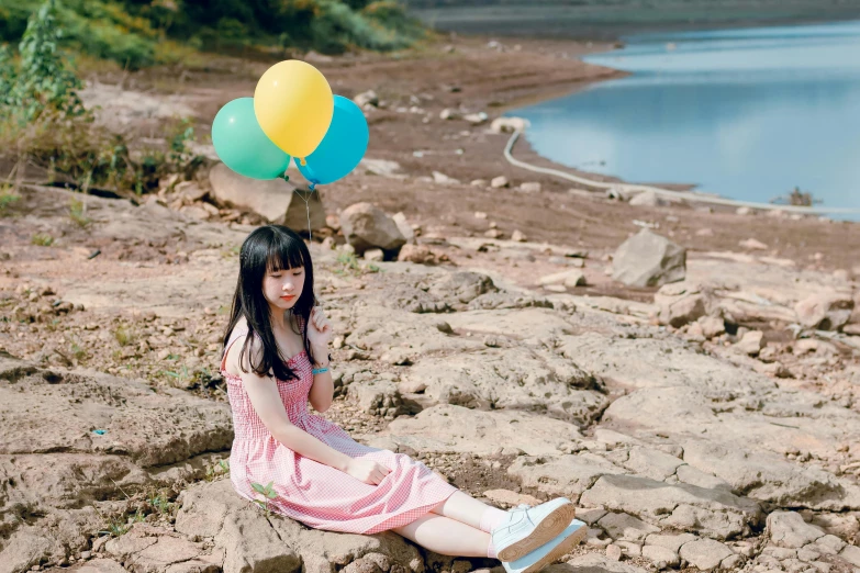 a woman sitting on a rock with a bunch of balloons on her head, by Tan Ting-pho, pexels contest winner, ulzzang, girl cute-fine-face, at the waterside, avatar image