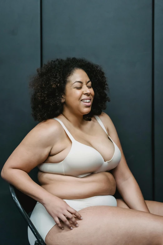 a woman in a white underwear sitting on a chair, slightly overweight, in a black betch bra, she is laughing, profile image