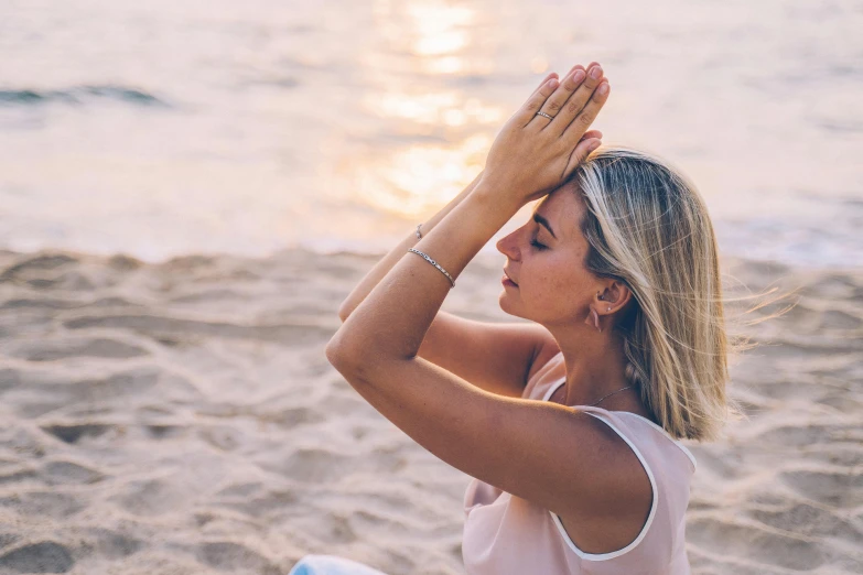 a woman sitting on top of a sandy beach, hands shielding face, connection rituals, in the morning light, profile image