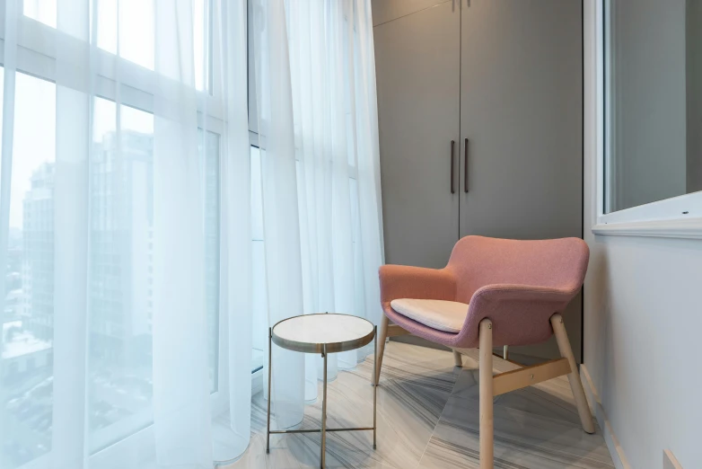 a chair sitting in front of a window next to a table, white and pink cloth, central hub, keng lye, grey