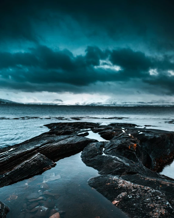 a body of water surrounded by rocks under a cloudy sky, ominous dark background, 5 0 0 px, reykjavik, trending photo