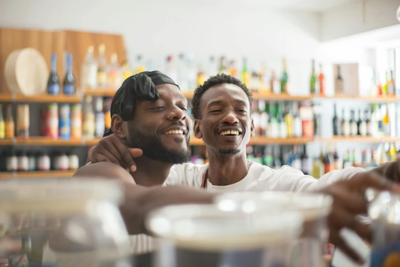 a couple of men sitting next to each other at a bar, a photo, trending on unsplash, brown skin man with a giant grin, two men hugging, milk bar magazine, beers on the table