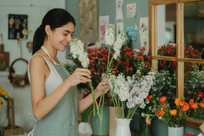 a woman standing in front of a bunch of flowers, a screenshot, pexels contest winner, arts and crafts movement, flower shop scene, wholesome, artist wearing overalls, an asian woman
