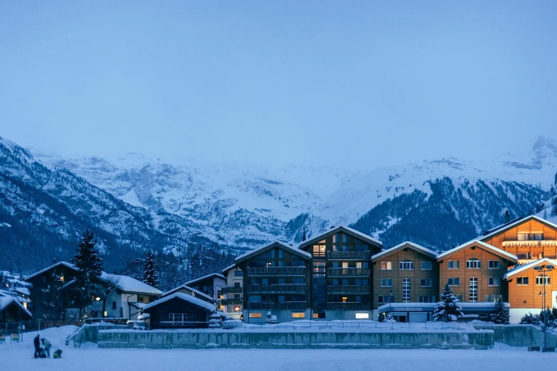 a group of buildings sitting on top of a snow covered slope, inspired by Peter Zumthor, pexels contest winner, blue hour, exterior, grand majestic mountains, grey