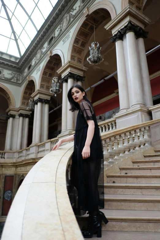 a woman in a black dress standing on a set of stairs, inspired by Modest Urgell, pexels contest winner, renaissance, dua lipa, pale skin, transparent, berlin fashion