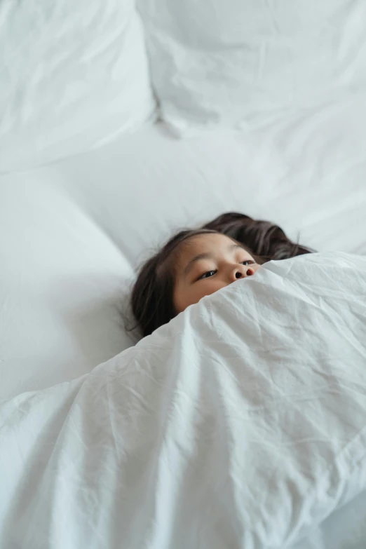 a woman laying on top of a bed covered in white sheets, pexels contest winner, happening, cloak covering face, kid, young asian girl, hibernation capsule close-up