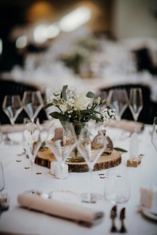 a bunch of wine glasses sitting on top of a table, flower decorations, looking towards the camera, elegantly dressed, slightly smiling