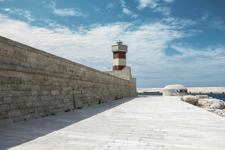 a red and white lighthouse sitting on top of a stone wall, by Carlo Martini, pexels contest winner, conversano, louis kahn, with walkways, hammershøi