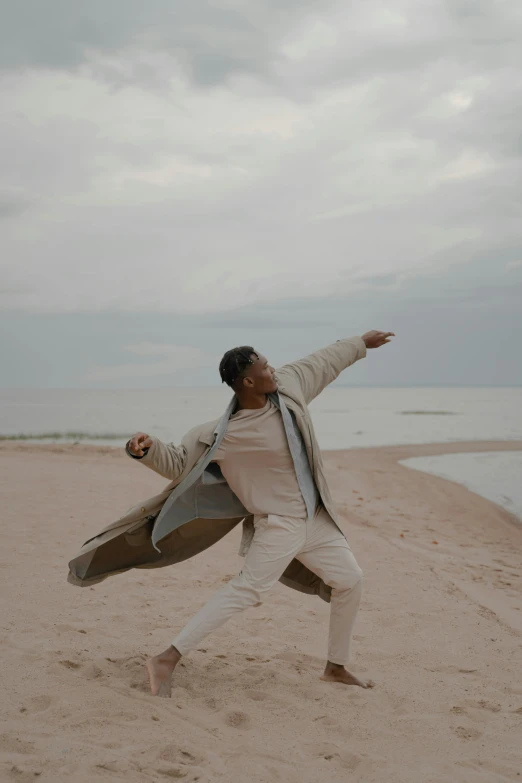 a man standing on top of a sandy beach, modern dance aesthetic, wearing a trenchcoat, doing a sassy pose, ryan jia