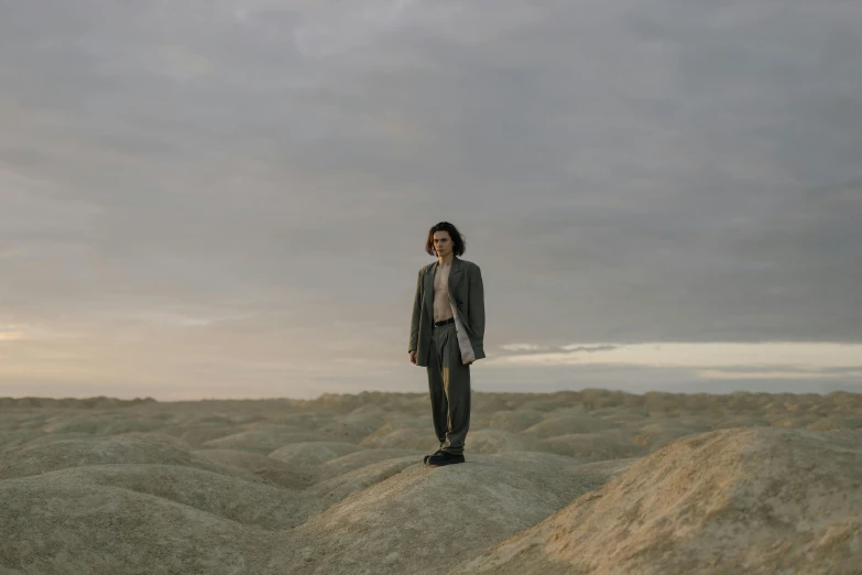 a man standing in the middle of a desert, by Elsa Bleda, surrealism, finn wolfhard, wearing a business suit, standing on rocky ground, lachlan bailey