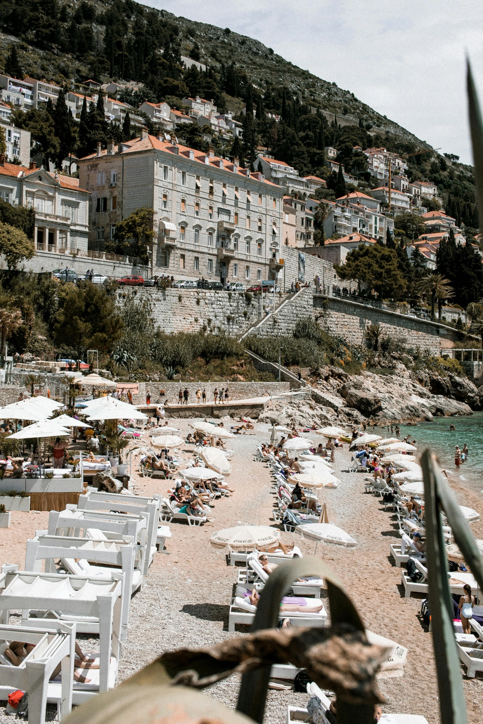 a group of people sitting on top of a sandy beach, umbrellas, white marble buildings, boka, an ocean