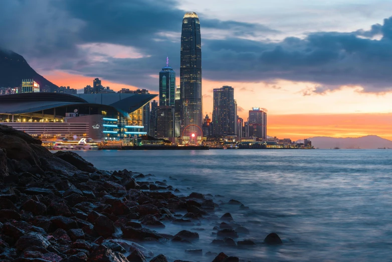 a large body of water with a city in the background, by Patrick Ching, pexels contest winner, sunset panorama, avatar image, street of hong kong, which shows a beach at sunset