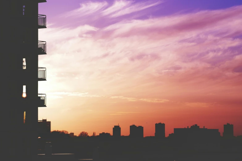 a tall building sitting next to a body of water, pexels contest winner, aestheticism, violet and yellow sunset, fire escapes, pastel palette silhouette, skyline view from a rooftop