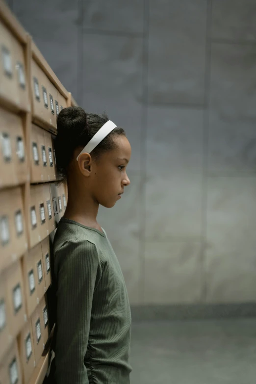 a little girl standing in front of a bunch of drawers, an album cover, inspired by Gordon Parks, pexels contest winner, side profile view, movie still 8 k, mixed race, in a ravaged library