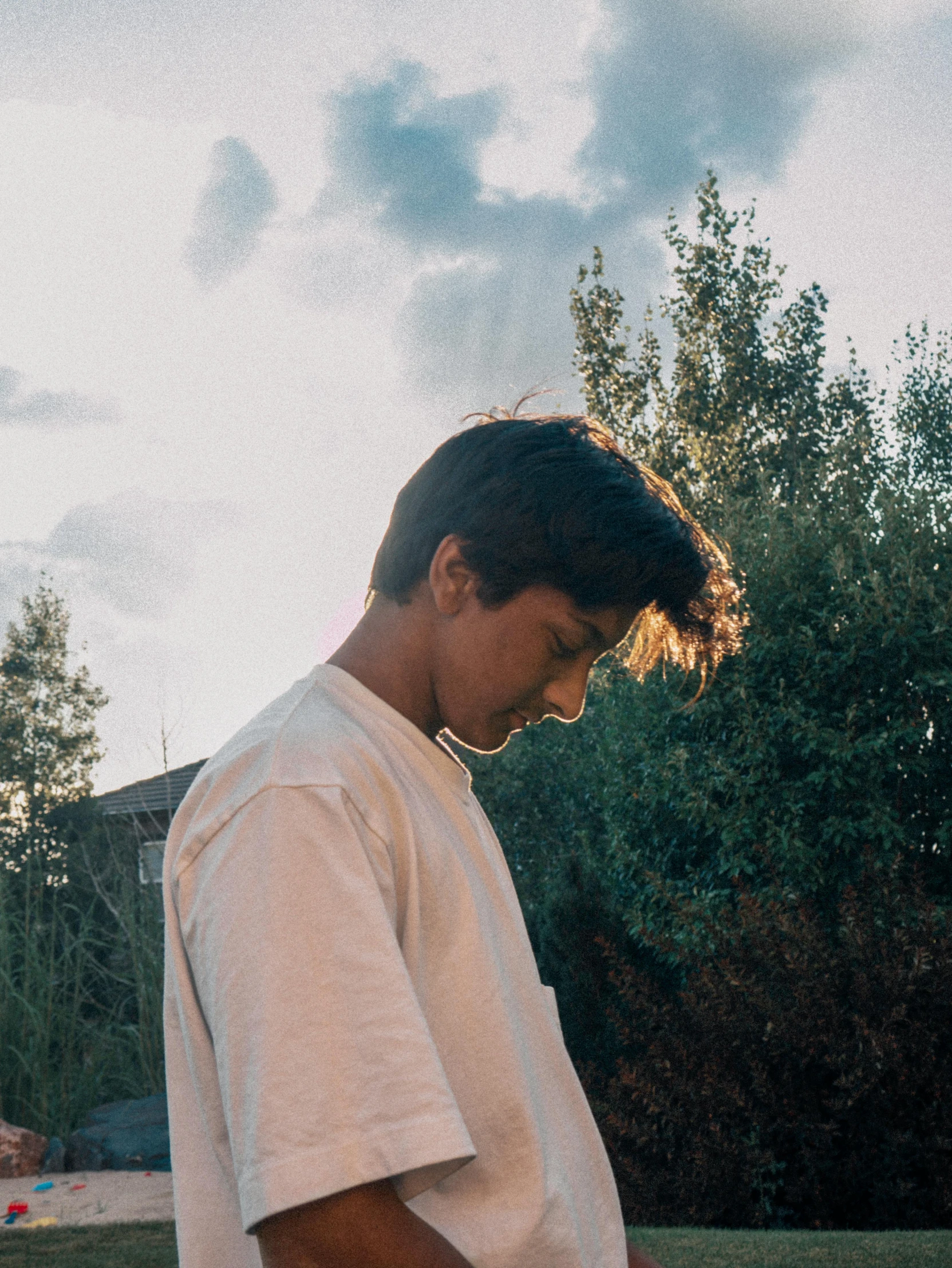 a man that is standing in the grass with a skateboard, an album cover, trending on unsplash, happening, soft evening lighting, 14 yo berber boy, profile image, wearing a white shirt