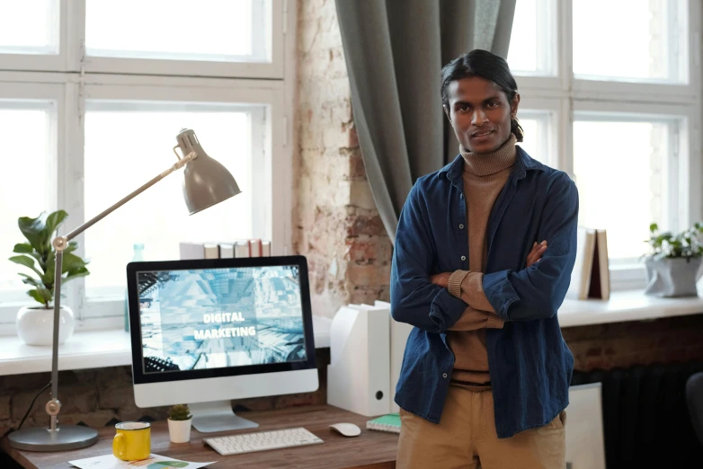 a man standing in front of a computer on a desk, a digital rendering, pexels contest winner, jayison devadas, looking to camera, vp of marketing, 9 9 designs