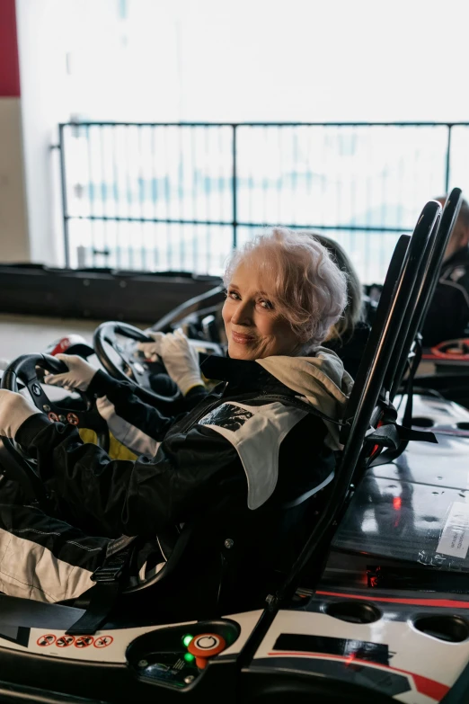 a woman that is sitting in a go kart, betty white, formula 1 garage, driving a car, profile image