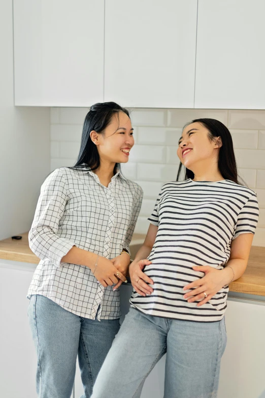 a couple of women standing next to each other in a kitchen, inspired by Ruth Jên, pexels contest winner, happening, pregnant belly, asian female, striped, profile image