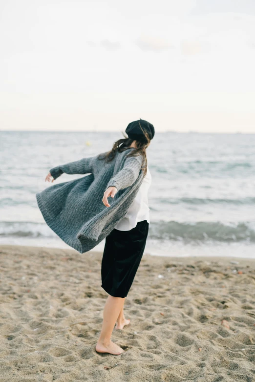 a woman standing on top of a sandy beach, unsplash, happening, wearing a cardigan, twirling, grey clothes, wearing an oversized sweater