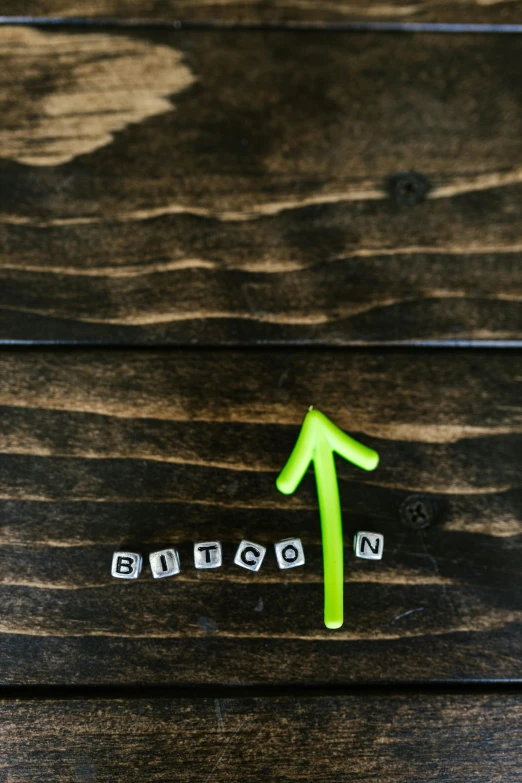 a green arrow sitting on top of a wooden table, bitcoin, thumbnail, word, digital image