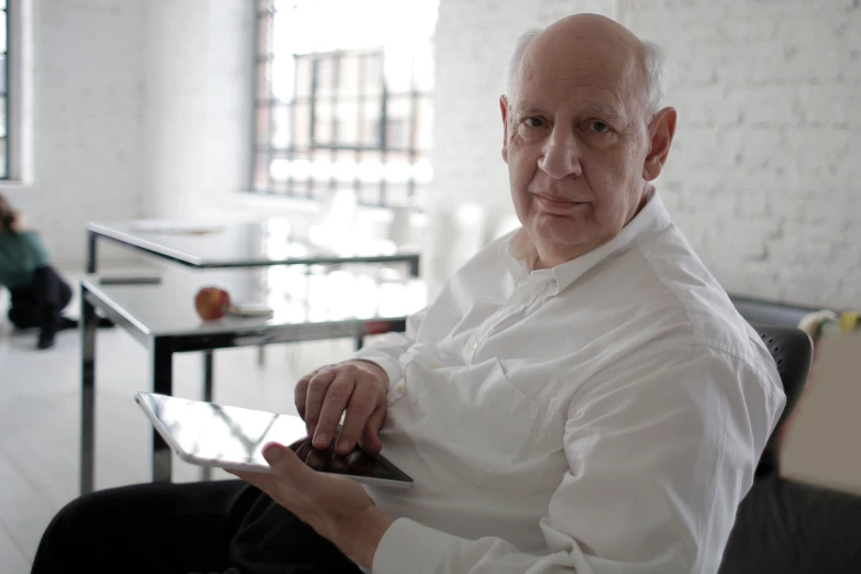a man sitting in a chair using a tablet computer, an album cover, inspired by Karl Ballmer, unsplash, hyperrealism, norman foster, looking towards camera, diana levin, on a white table