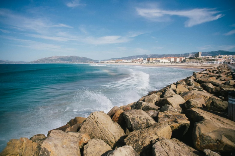 a beach filled with lots of rocks next to the ocean, unsplash contest winner, les nabis, the sea seen behind the city, la nouvelle vague, long beach background, hills and ocean