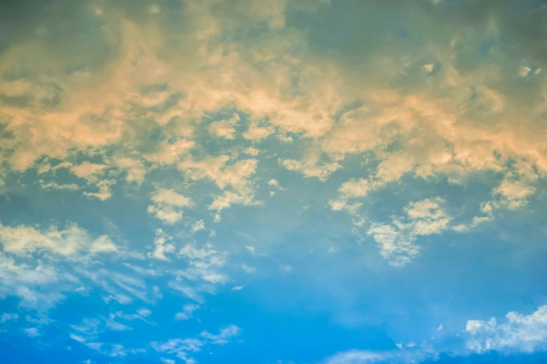 a plane flying through a cloudy blue sky, an album cover, inspired by Elsa Bleda, unsplash, romanticism, orange and blue colors, layered stratocumulus clouds, yellow and blue and cyan, looking upwards
