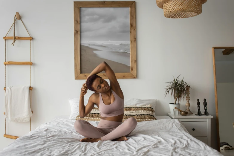 a woman sitting on top of a bed in a bedroom, by Sam Charles, trending on pexels, happening, two piece workout clothes, serpentine pose gesture, pink zen style, with brown skin