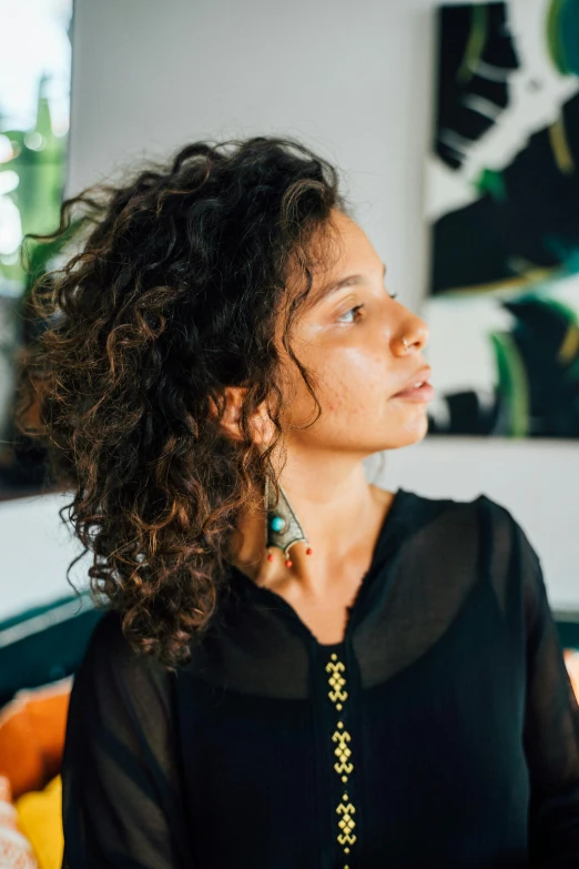 a woman sitting on a couch in a living room, by Lily Delissa Joseph, pexels contest winner, renaissance, curly middle part haircut, giant earrings, headshot profile picture, brazilian